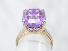 This stunning vintage amethyst ring has a pretty medium-hued purple amethyst in the center, that really flashes and flickers with vibrant violet reflections! Set into a lovely retro era mounting with structurally designed diamond shoulders and simple corner prongs, this vintage ring is a beautiful addition to anyone’s collection!Metal: 14K Yellow and White GoldGem: Amethyst 9.81 CaratsGem Measurements: 15.3 x 11.2 mm, Emerald CutAccents: 6 Diamonds totaling .06 Carats, SI2 in Clarity, K in ColorRing Size: 5.75Marks: “14K” Stamped on the inside band Vintage Amethyst Ring, Channel Set Diamond Band, Amethyst Ring Vintage, Retro Era, Diamond Accent Ring, Amethyst And Diamond Ring, Engagement Ring Diamond Cut, Tanzanite Ring, Diamond Cocktail Rings