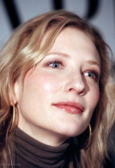 a close up of a woman with blonde hair and blue eyes wearing gold hoop earrings