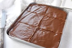 a pan filled with brownies on top of a white cloth next to a knife and fork