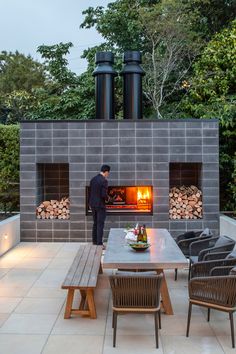 a man standing in front of an outdoor fireplace with chairs around it and tables on either side