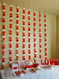 valentine's day dessert table with paper hearts on the wall