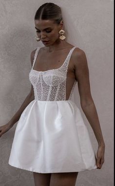 a woman in a short white dress is holding her hand out and looking down at the ground