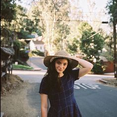 a woman wearing a hat standing on the side of a road with her hands behind her head