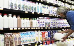 a woman is picking up milk from the shelf in a grocery store while looking at it