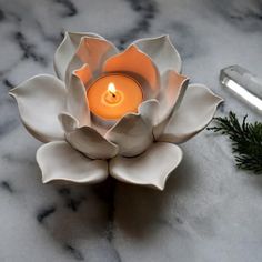 a lit candle sits in the center of a white flower on a marble countertop