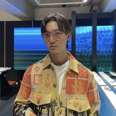 a young man wearing glasses standing in front of desks with blue and yellow wallpaper