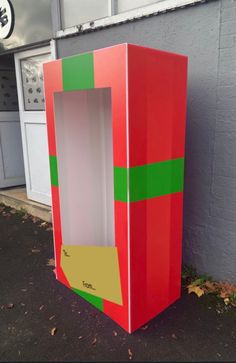 a red and green cardboard box sitting in front of a building