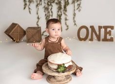 a baby sitting on the floor with a cake in front of him and one sign behind it