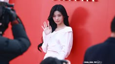 a woman standing in front of a red wall holding her hand up to the side