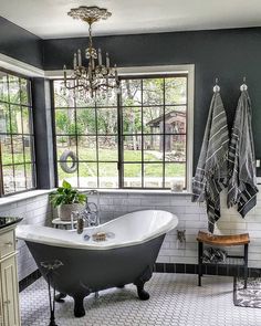 a bathroom with a claw foot tub and chandelier hanging from the ceiling in front of two windows