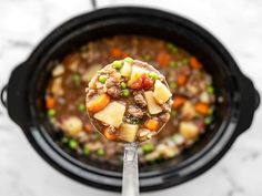 a spoon full of stew in a crock pot with peas, carrots and potatoes