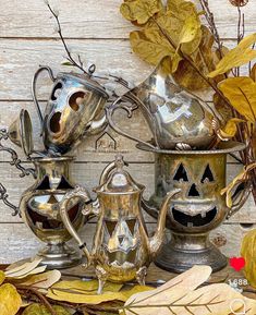 an assortment of metal teapots with faces painted on them and leaves around them