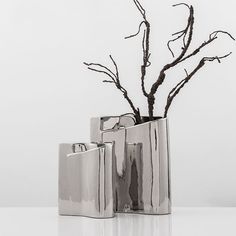 three silver vases with branches in them on a table