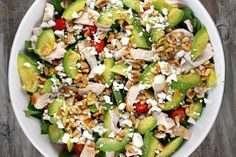 a salad with chicken, avocado and feta cheese in a white bowl