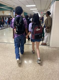 two people walking down an airport hallway with backpacks on their backs and one person holding the other's hand