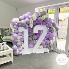 the number twelve is made out of balloons and white hydrangeas in front of a living room door