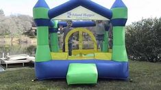 an inflatable bouncer with two people on it sitting in the grass next to a body of water