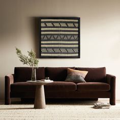 a living room with a brown couch and coffee table in front of a painting on the wall