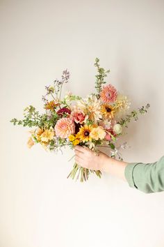 a person holding a bouquet of flowers in their hand against a white wall with no one around it