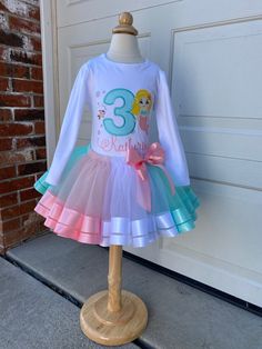 MERMAID PASTEL MULTICOLOR TUTU SET.  The shirt features a glitter canvas along with a cute mermaid, the design on the shirt is embroidered meaning is stitched onto the shirt for durability and quality. The backing on the design will help to keep that area soft against the child skin. The shirt is a boutique quality t-shirt, thick and very soft, run true to size (see size chart), and range from 12m-12, also bodysuits available sizes 6m-18m Colors can be customized please just include it in the message. Tutu is a poly or nylon tulle with double face ribbon trims. PROCESSING TIME IS CURRENTLY 1-2 WEEKS FROM DATE OF PURCHASE. Processing time do not include shipping, which is an additional 2-5 business days. If needed sooner, a rush upgrade can be chosen during check out for an additional cost; Ribbon Trim Tutu Size Chart, Tutu Size Chart, Easter Tutu, Mermaid Tutu, Ribbon Trim Tutu, Princess Outfit, Rainbow Tutu, Glitter Canvas, Toddler Easter