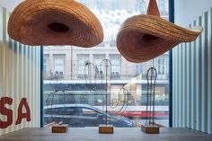 two large woven hats hanging from the ceiling in front of a window with cars passing by