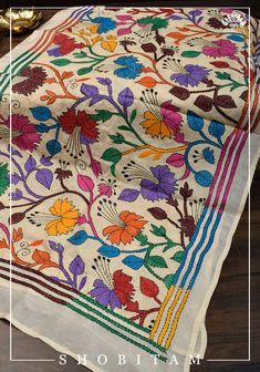 an embroidered cloth with colorful flowers and leaves on it, sitting on top of a wooden table