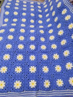 a blue crocheted blanket with white and yellow flowers