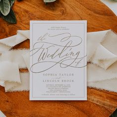 the wedding stationery is laid out on a wooden platter with white napkins and greenery