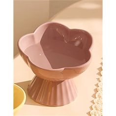 a pink heart shaped bowl sitting on top of a table next to a yellow cup