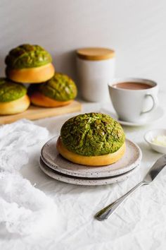 there is a green pastry on the plate next to some coffee cups and spoons