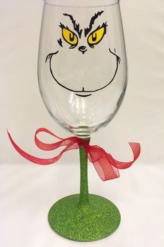 a wine glass with an angry grin face painted on the side and a red ribbon around it