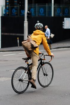 a man riding a bike down the street with a backpack on his back while wearing a yellow jacket