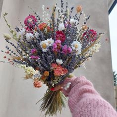 a hand holding a bouquet of flowers in front of a building with a sky background