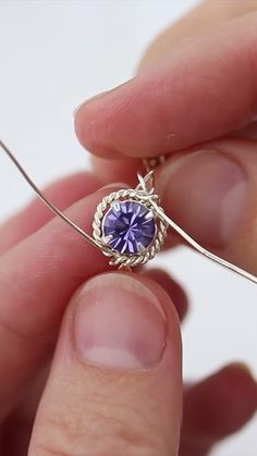 a person is holding a wire with a purple stone in it's center,