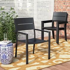 two black chairs sitting on top of a rug next to a brick wall and potted plant