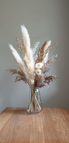 a glass vase filled with dried flowers on top of a wooden table