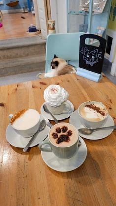 there are three cups of coffee on the table and one has a cat's paw in it