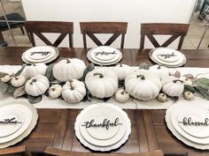 a dining room table with white pumpkins and greenery on the place settings for thanksgiving dinner