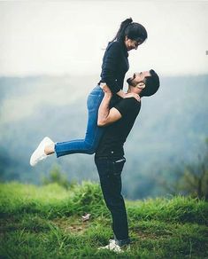 a man carrying a woman on his back in the air while standing on top of a lush green hillside