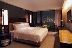 a hotel room with a large bed, desk and window overlooking the city at night