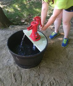 a woman is pouring water from a red pump into a black bucket on the ground