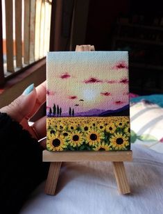 a person is holding up a small canvas with sunflowers on it