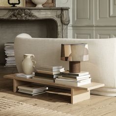 a living room with a couch, coffee table and books on the floor in front of a fireplace