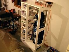 a white cabinet filled with lots of shoes next to a table and chair in a room