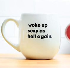 a white coffee mug with words on it sitting on a table next to a red cup