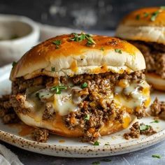 two cheeseburger sliders on a plate with sauce and green garnish