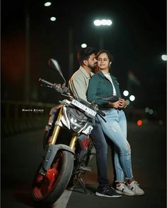 a man and woman sitting on top of a motorcycle at night with their arms around each other