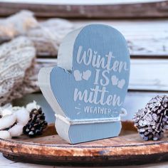 a wooden sign that says winter is matten weather on it next to pine cones