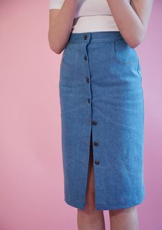 a woman standing in front of a pink wall wearing a blue skirt and white shirt