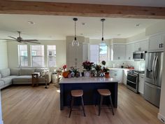 an open kitchen and living room with white walls, wood flooring and stainless steel appliances